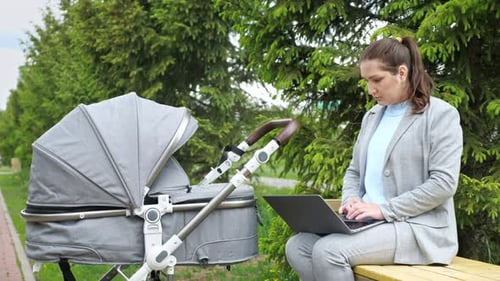 Mother Freelancer Works on Laptop Calming Baby in Stroller