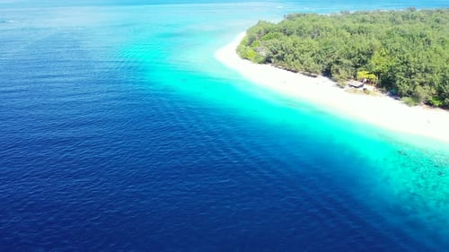 Blue sea and turquoise lagoon surrounding white sand of pristine beach of tropical island with trees