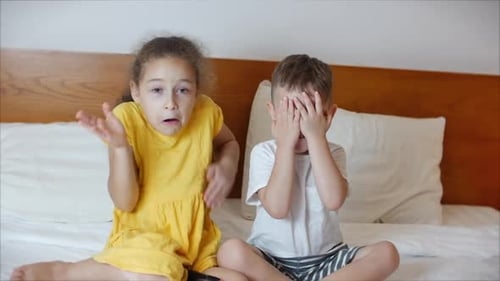 Girl and Boy Sitting on Bed Covering Eyes