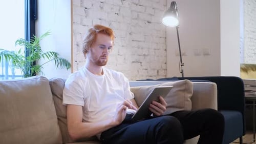 Kreativer Designer beim Surfen im Internet auf Tablet PC, Auf Couch sitzend