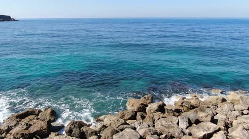 Die Kamera bewegt sich von der felsigen Küste entlang türkisblauer Wellen, die im Sonnenschein Seelandschaft von