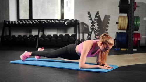 Young woman is training in the gym. In the plank, he does an exercise on the abs