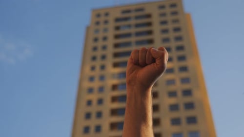 Raised Fist Against Urban Building and Blue Sky
