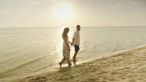A Young Couple Is Walking By the Sea Under a Summer Rain at Sunset