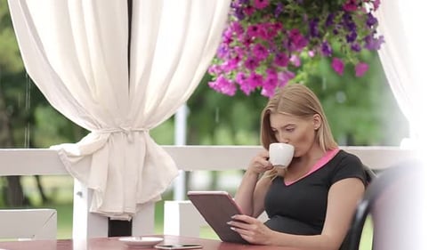 Beautiful girl with light hair wearing colorful shirt sitting in cafe with tablet