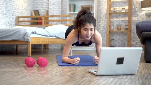 Asiatische Frau in Sportbekleidung trainiert, während sie sich online einen Fitnesstrainingskurs auf dem Laptop ansieht