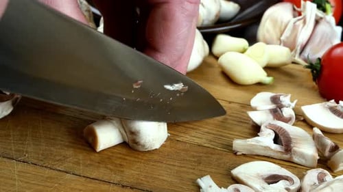 Essbare Champignons werden mit einem scharfen Messer auf einem Küchenbrett aus Holz geschnitten