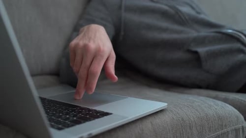 Cara cansado digitando lentamente em seu computador enquanto está sentado no sofá