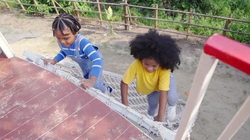 4K Little African boy and girl climbing rope net together at outdoor playground in the park