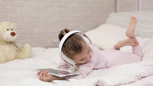 Girl Uses Tablet on Bed with Headphones