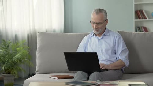 Senior Man Using Laptop on Couch Indoors