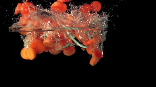Karottenstücke in Superzeitlupe fallen mit Spritzern ins Wasser