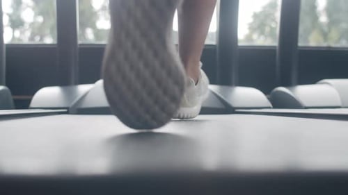 Un joven asiático con los pies en zapatillas hace ejercicio corriendo en una cinta de correr para quemar grasa en la clase de acondicionamiento físico.