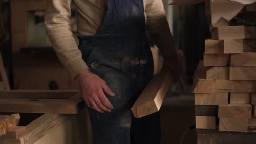 The Carpenter in the Workshop Goes to the Grinding Machine with a Bar of Wood