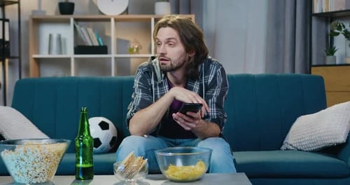 Bored Man Sits at Home with Smartphone