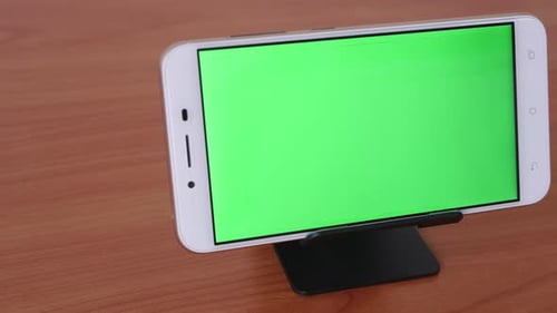 Slide motion of The green screen phone is placed on a pedestal on a wooden table.