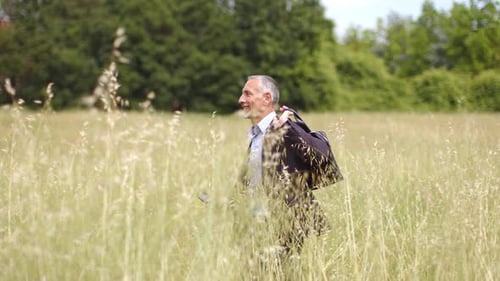 Lächelnder Geschäftsmann mit Smartphone und Aktentasche läuft auf Wiese