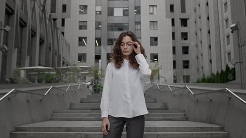 Young Girl Dressed In Business Style Clothes Stands On The Background Of Tall Building
