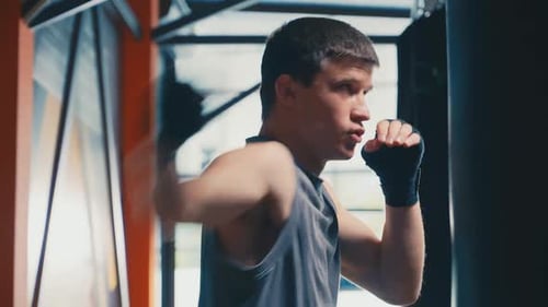 Young Adult Man Punches Boxing Bag in Gym