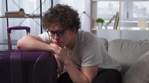 Young Adult Resting Head on Suitcase at Home