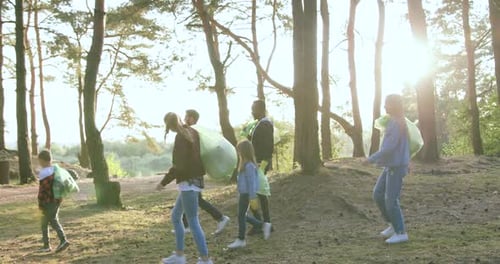 Voluntarios activos y diversos con bolsas de basura abandonan el parque después de la limpieza otoñal