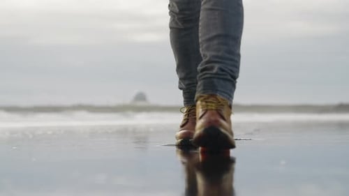 Man In Hiking Boots Walking Towards Camera Over Wet Beach