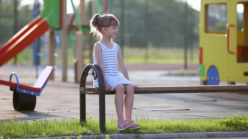 Cute Child Girl Waiting for Her Mother Sitting on a Bench on Summer Playground in Kindergarten Yard