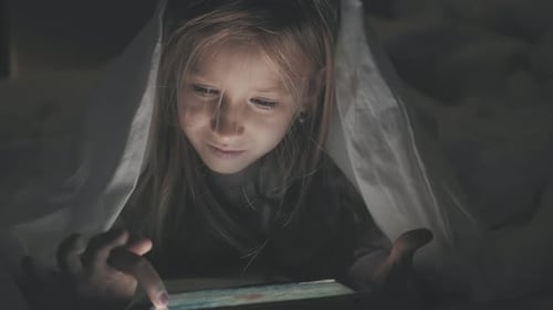 Adolescente au lit jouant sur une tablette sur Internet social dans la pénombre. Gros plan d'une petite fille