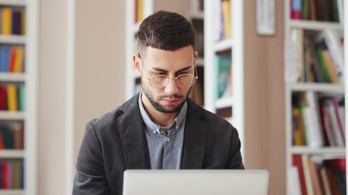 Man in Eyeglasses Working on Laptop in Library