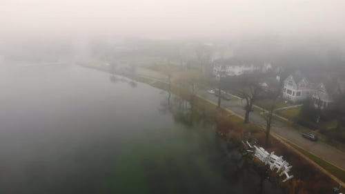 Aerial Flying Over the Lake in Heavy Fog and Cloudy Weather. The Embankment of the Lake on a Foggy