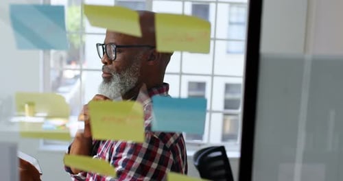 Adult Thinking in Front of Glass Whiteboard in Office