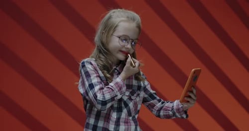 Girl Applies Lipstick While Looking at Phone