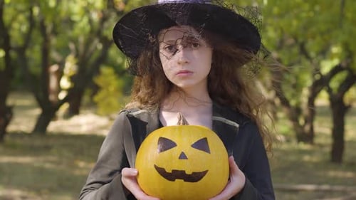 Seriously Looking Redhead Caucasian Girl Dressed in Halloween Witch Costume Standing in the Autumn