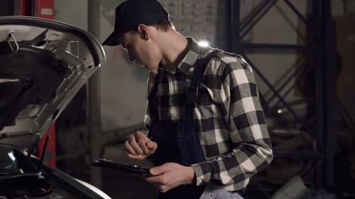 Man Working on Car Using Tablet in Garage