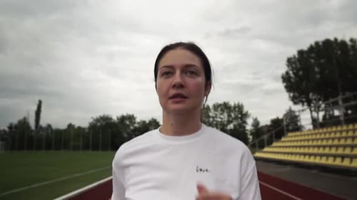 Young woman is running in the stadium. woman with white sweater and black tights. Camera follows run