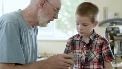 Grandfather Teaches Young Boy Woodworking Skills Indoors