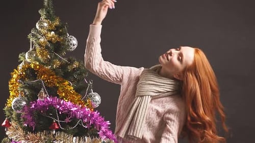 Retrato de una niña pelirroja bailando suavemente cerca del árbol de Navidad en el estudio sobre fondo negro