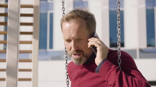 Man Smiling and Talking on Phone on Swing