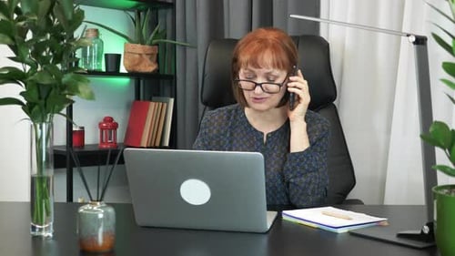 Woman Working at Desk Talking on Phone and Writing Notes