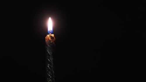 Eine einzelne Kerze wird auf einem schwarzen Hintergrund angezündet. Kerzenflamme im Dunkeln.
