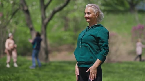 Positive Slim Female Retiree Bending Forward Smiling Working Out in Sunny Summer Spring Park