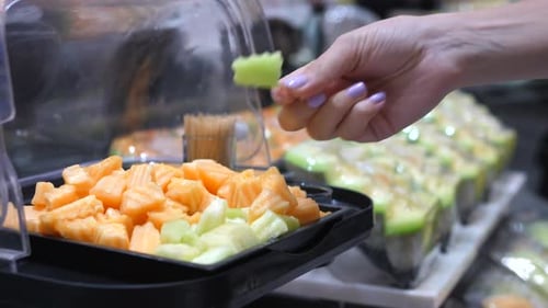 Une cliente essaie à la main du melon fraîchement coupé en dés au supermarché