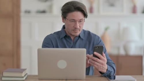 Man using Smartphone while using Laptop in Office