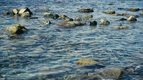 Gentle Waves Lapping at Rocky Shoreline on Sunny Day