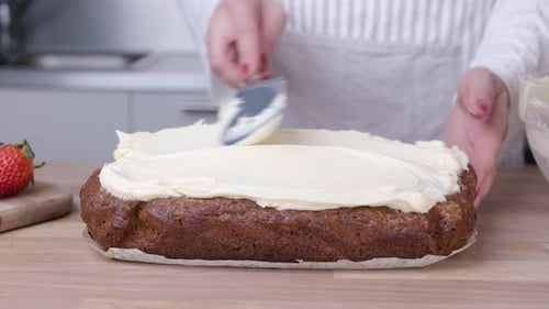 Bäcker verteilt Zuckerguss auf Karottenkuchen mit Spatel. - Schieber links