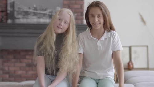 Two Smiling Young Girls Sitting Together Indoors