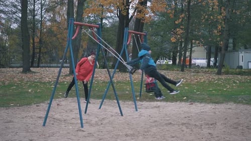 Happy Boy and Girl is Swaying on Swing in Park at Autumn Day and Jumping Out in Slow Motion.