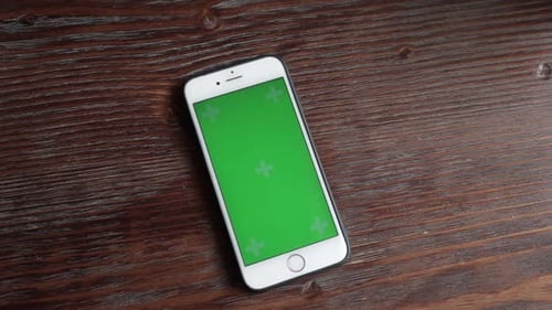 Mobile Phone with a Green Screen on a Brown Wooden Table