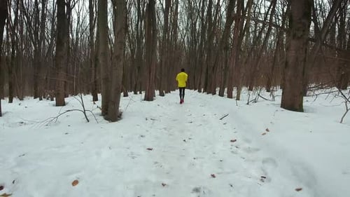 Back of Male Runner in Yellow Coat in Winter Forest