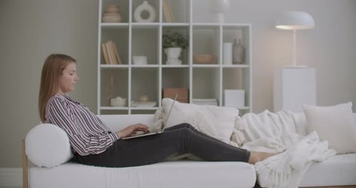 Woman Relaxes with Laptop on White Sofa